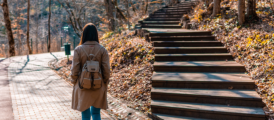 Girl with long coat, backpack at crossroads of stair path and brick path in wood