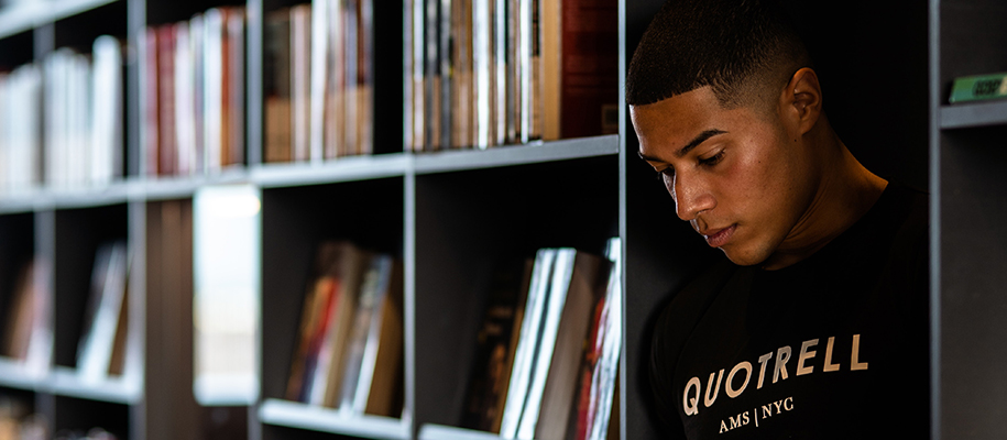 Young man in black T-shirt standing between bookshelves with books behind him