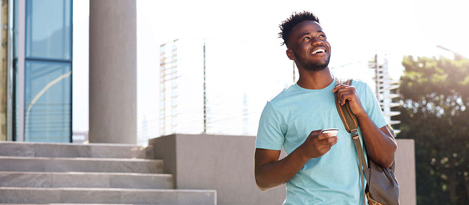 Black male college student smiling and holding phone walking down stairs outside