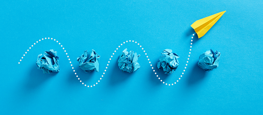 Crumpled balls of blue paper with paper airplane dodging them on blue backdrop