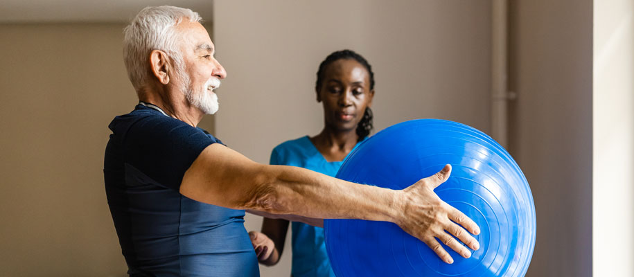 Black female nurse at senior center doing physical therapy exercises with man