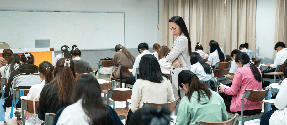 Classroom full of students, heads down, taking a test while teacher observes