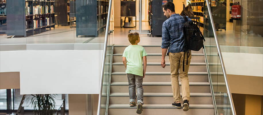 White male teacher in blue plaid and White boy in green walk up library stairs