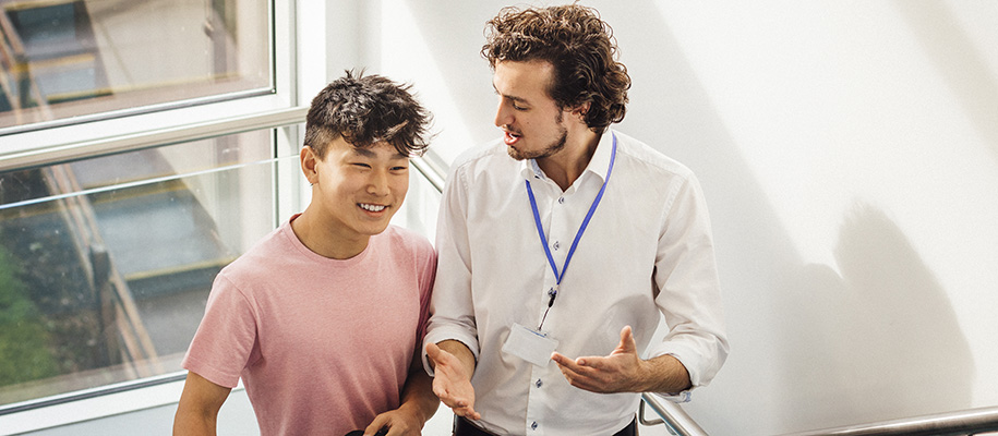 Young White male teacher walks up school steps with Asian male teen