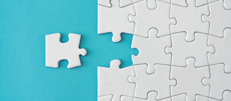 Loose white jigsaw puzzle piece next to completed puzzle on blue background