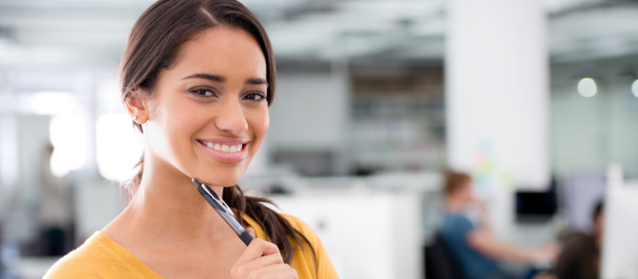 Black female with straight brown ponytail smiling in office with pen to chin