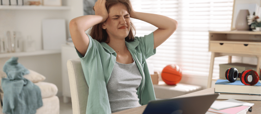 A young woman has her hands pressed against her head with a stressed face