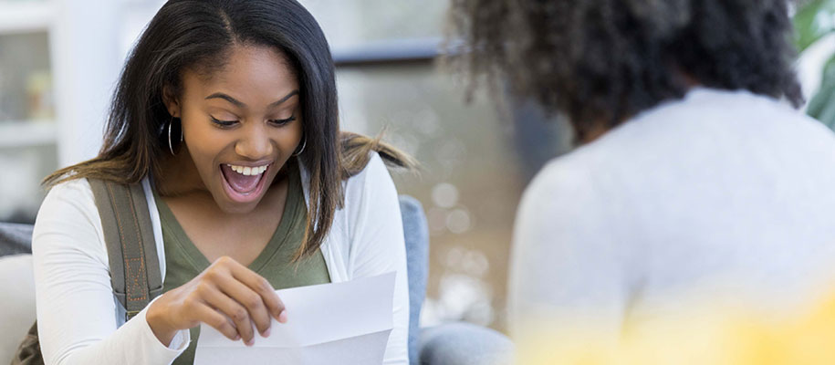 Black female student opening letter looking excited with counselor