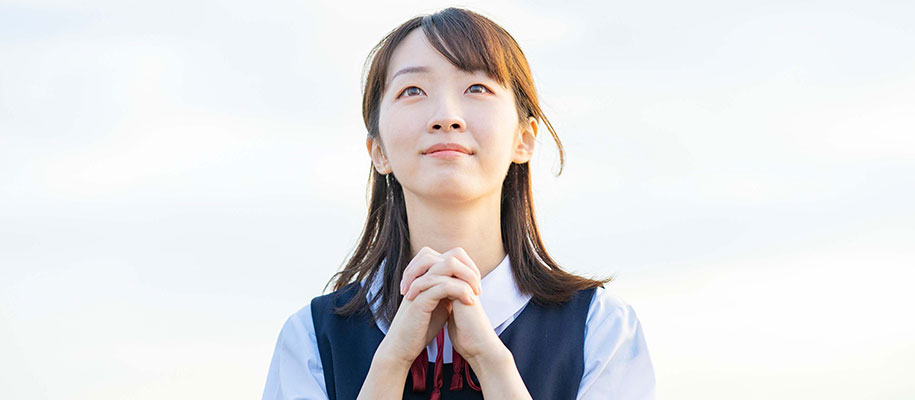 Asian female in Catholic school uniform holding hands in prayer, looking at sky