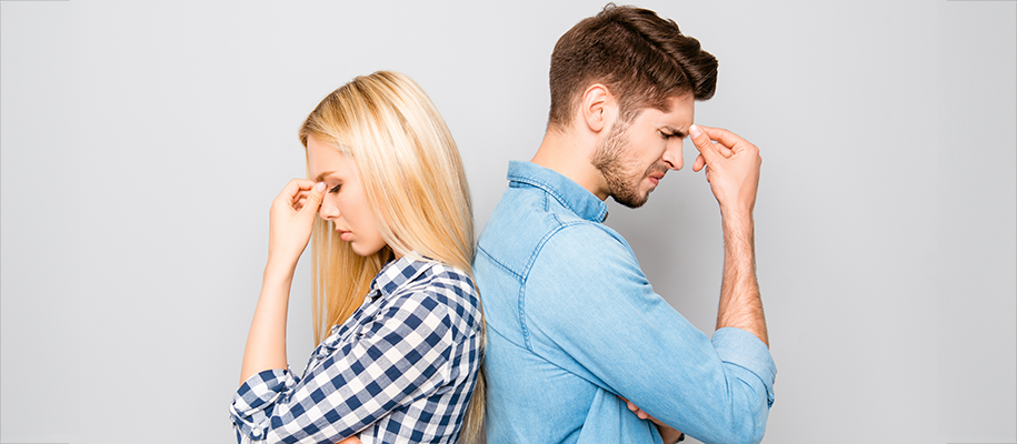 White blond woman with back against White man, both stressed with hands to face