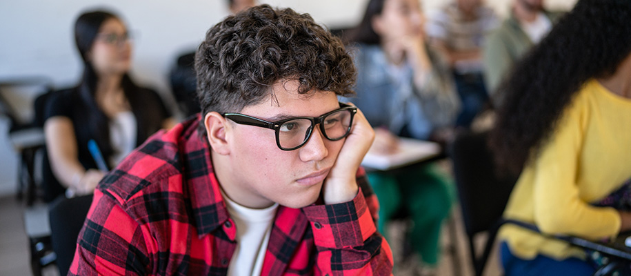 Hispanic teen in red plaid and glasses, head in hand bored in high school class