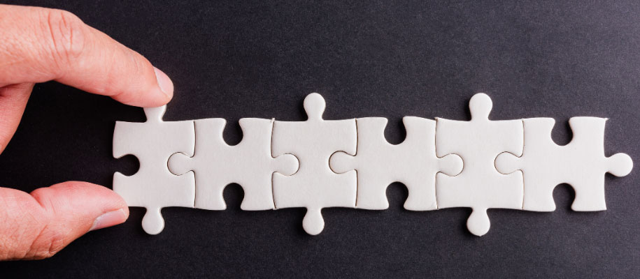 Closeup of White hand holding white puzzle piece, connecting six pieces total