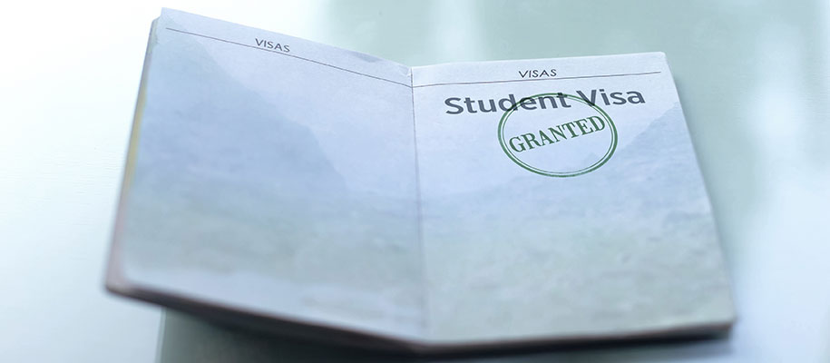 Open passport on table with words Student Visa at top and Granted stamped on it