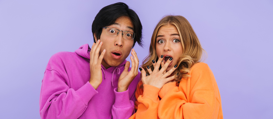 Asian man in purple and White woman in orange sweatshirts looking shocked