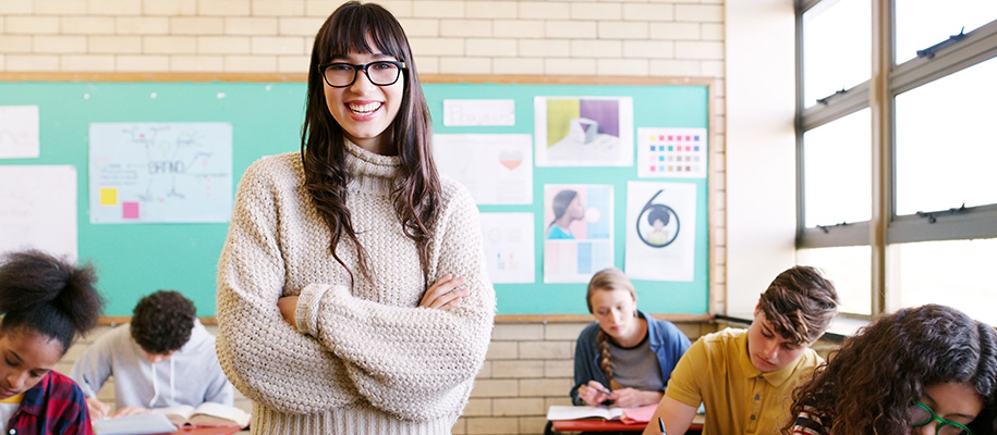 Cheerful young White teacher in sweater, smiles in class with students at desks