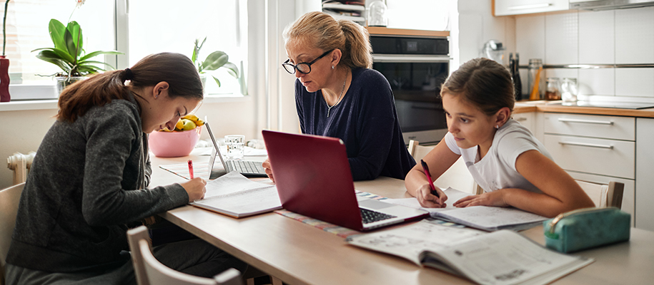 White blond mom with glasses homeschooling teen and young daughters in kitchen