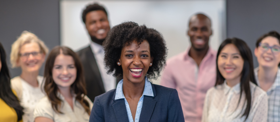 Black woman in business suit smiling at camera, career team grouped behind her