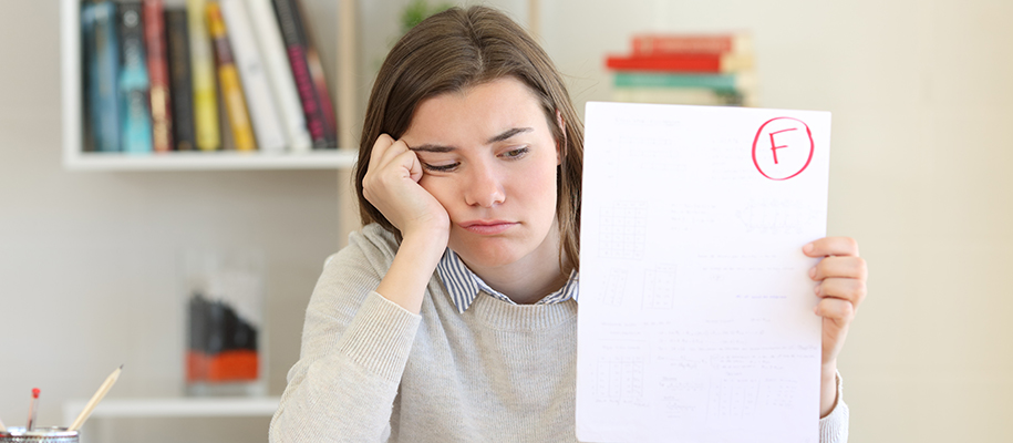 Student in sweater, collared shirt holding up test with F, hand on face upset