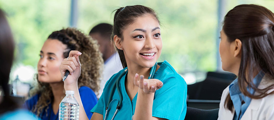 Female medical student in scrubs talking with other students in classroom