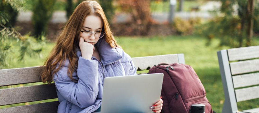 Redhead female in glasses, sitting on bench with laptop, thinking deeply