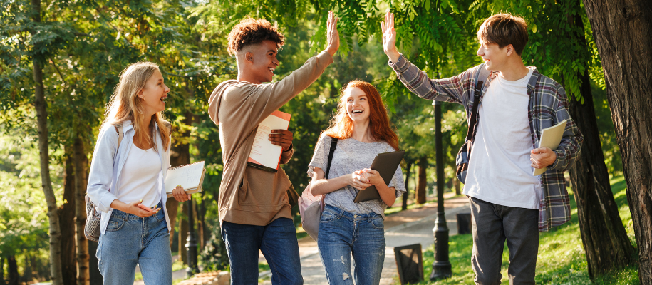 Four young undergraduates on campus with men high-fiving and women laughing