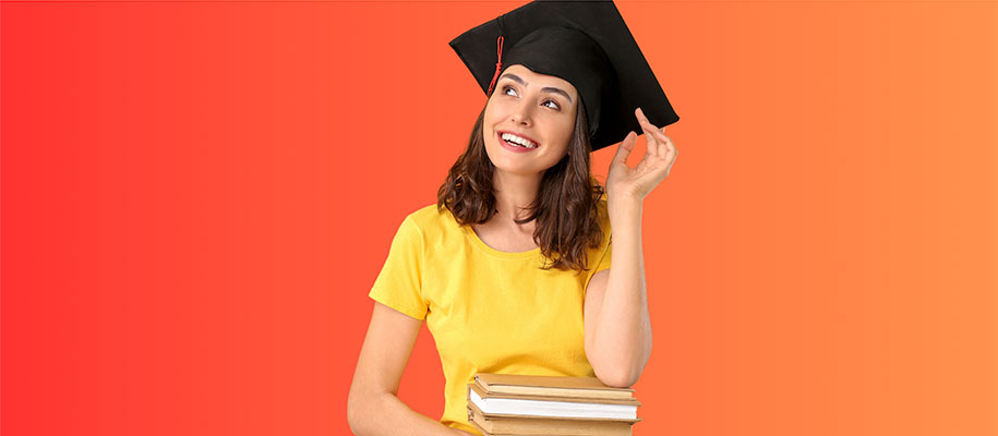 White brunette in yellow tee and black graduation cap, holding books, smiling