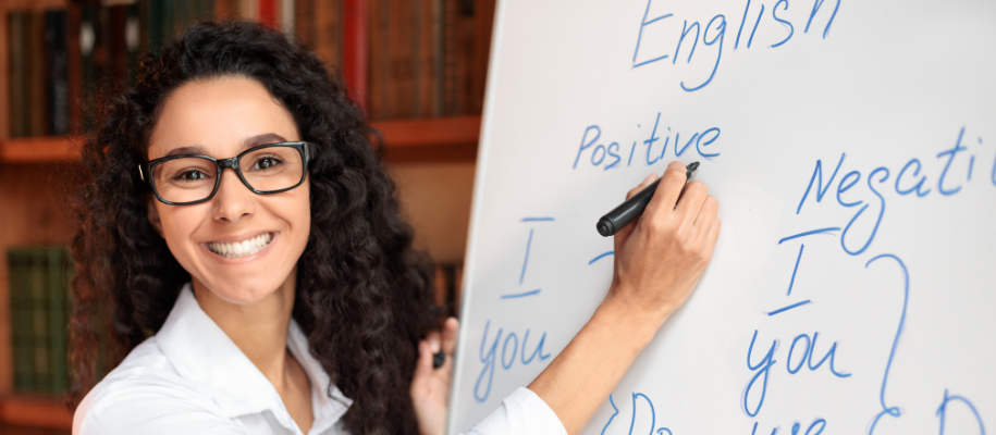 Smiling female English teacher at whiteboard, explaining grammar lesson