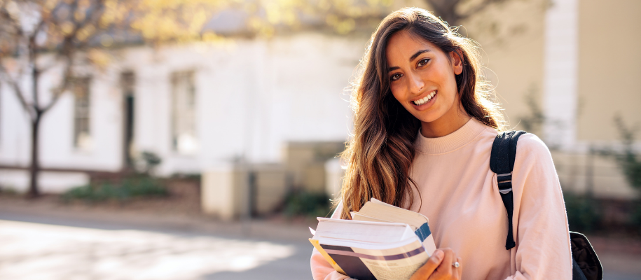 Latina student on college campus looking happy with books, backpack