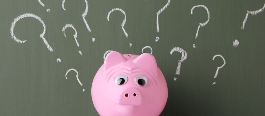 Pink piggy bank with large googly eyes by chalkboard with many question marks