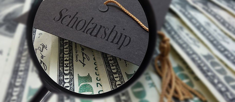 Graduation cap reading Scholarship under magnifying glass with $100 bills