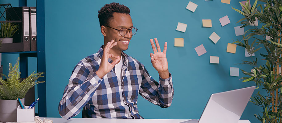 Happy Black male in plaid shirt & glasses looking at laptop, giving 2 OK symbols