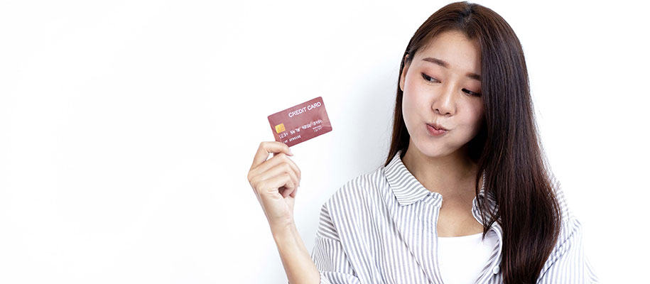 Young Asian woman holding credit card in one hand, giving it the side eye
