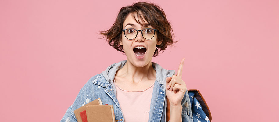 Excited female student in denim holding books, pointing finger up with new idea