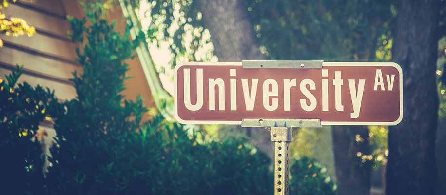 Brown street sign with University Av on sunny day in front of trees and house