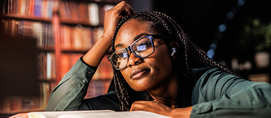 Black woman with braids, glasses, wireless ear pods, looking stressed in library