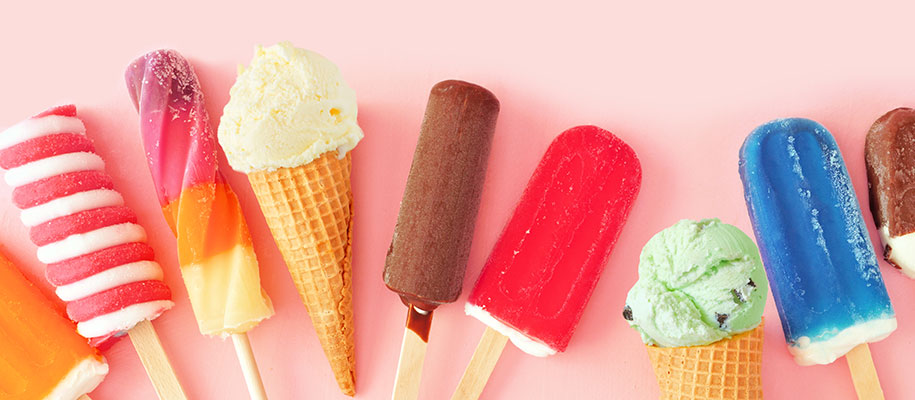 Various colorful ice cream cones and popsicles lying against orange background