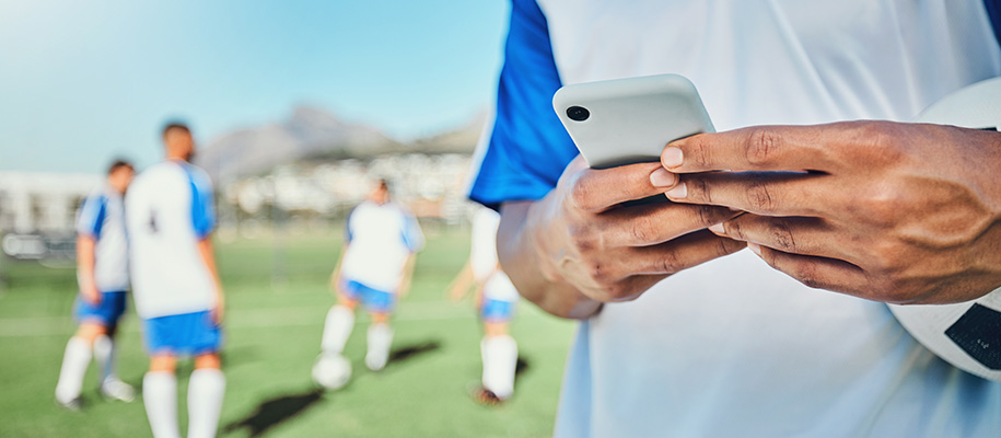 Hands of Hispanic young man typing on phone, soccer team in background