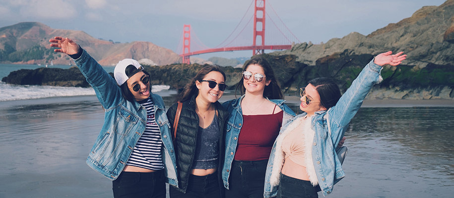 Four young women smiling, laughing on beach by Golden Gate Bridge