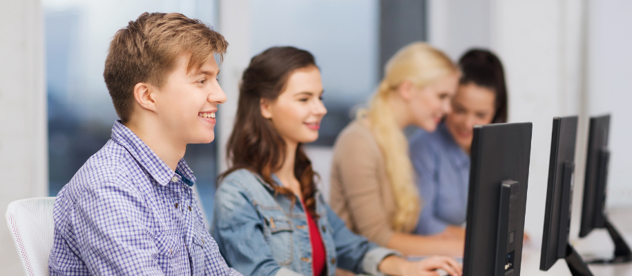 Focus on male student at computer in row of computers with three girls