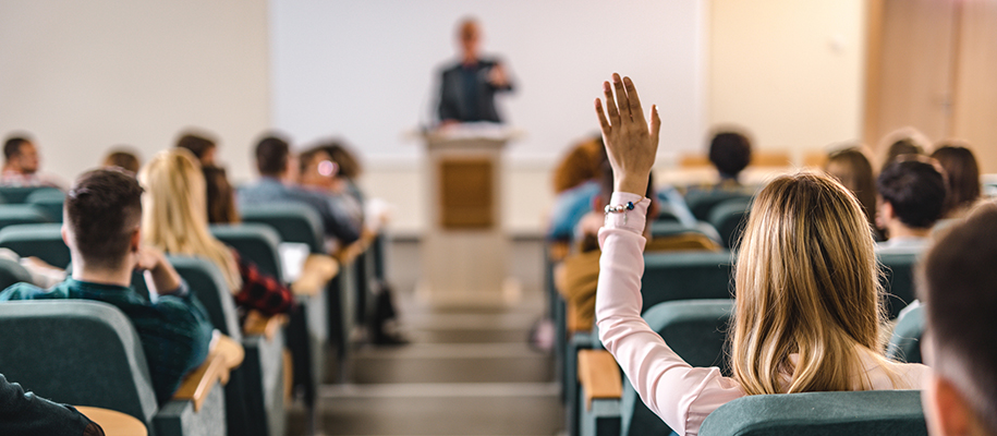 Lecture hall from beyond, focusing on White woman raising hand on right side