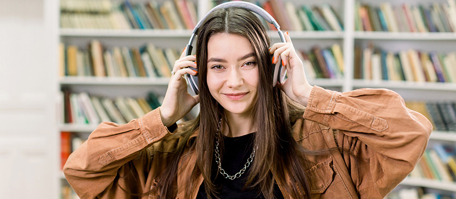 Young White brown-haired woman in corduroy shirt puts on headphones in library