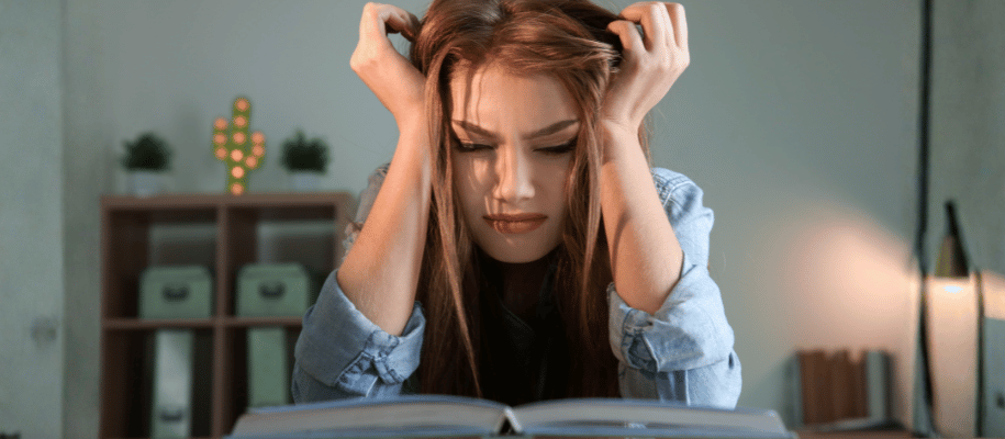 Young woman with hands in her hair, stressed face, looking over a textbook
