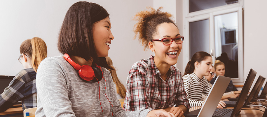 Asian woman smiling with Black woman in red glasses in women's coding lab