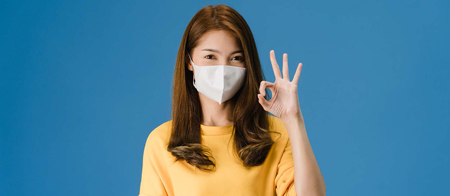 Asian woman in yellow shirt holding up okay with fingers, wearing face mask