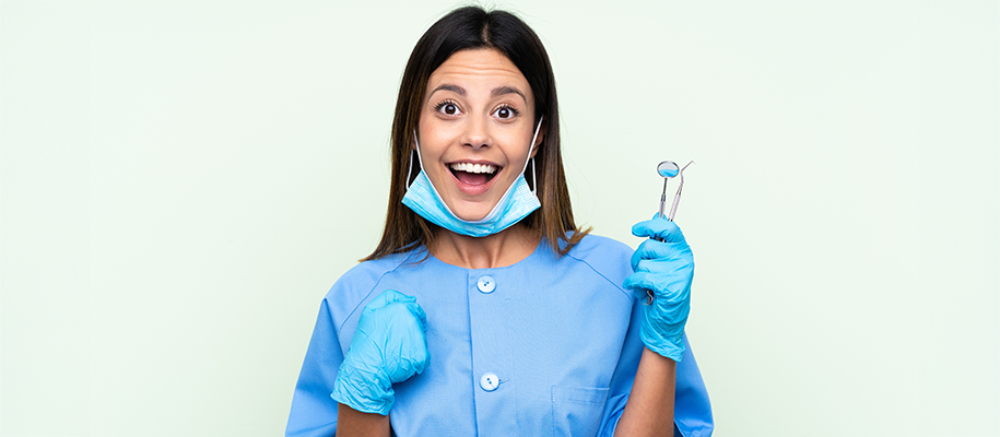 Surprised White woman in dentist scrubs with face mask down, gloves, equipment