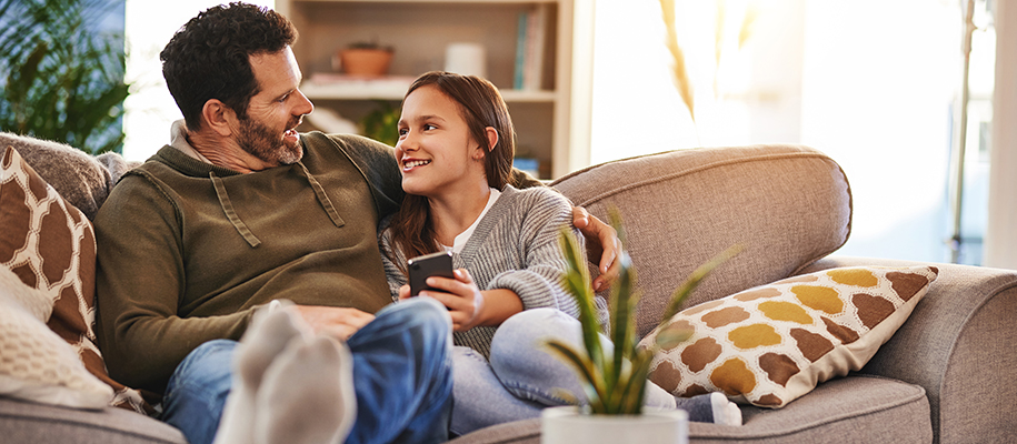 Father with arms around daughter on couch, who’s showing something on phone