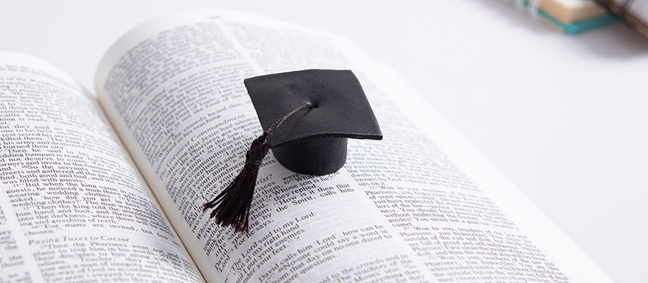 Small black graduation cap on top of page of open Bible