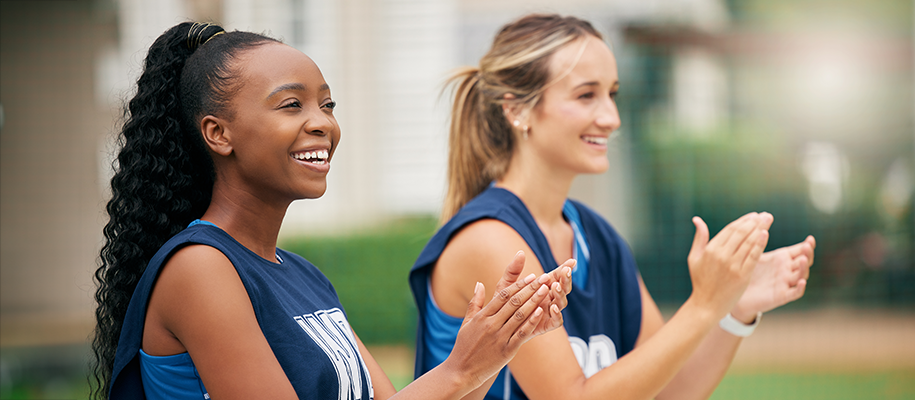 Black and White young women in blue sports jerseys smiling and clapping outside