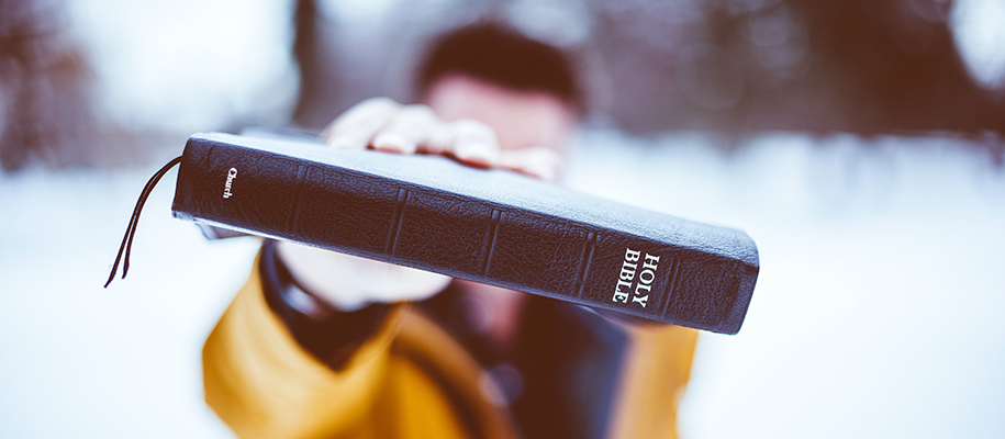 Out-of-focus White man in a yellow jacket out in snow holding Bible up to camera
