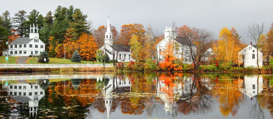 Four white church buildings on banks of small link, reflections in water in fall